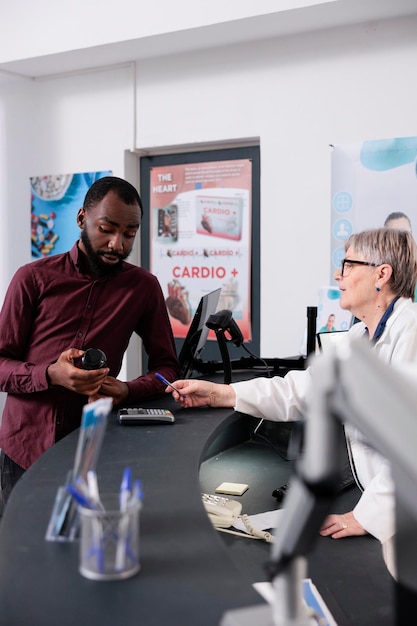 Employé de pharmacie senior debout au comptoir de la pharmacie aidant le client avec un traitement pharmaceutique après avoir vérifié la prescription médicale, discutant de la notice des pilules. Service de soins de santé et soutien