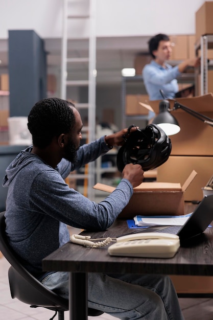 Employé regardant le casque vérifiant l'état du produit avant la livraison du colis au client, vérifiant les détails d'expédition du client sur un ordinateur portable. Gestionnaire afro-américain travaillant dans un entrepôt