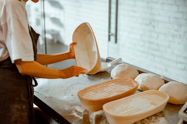 L'employé répand la farine à l'intérieur du plat pour le pain dans l'atelier léger de boulangerie