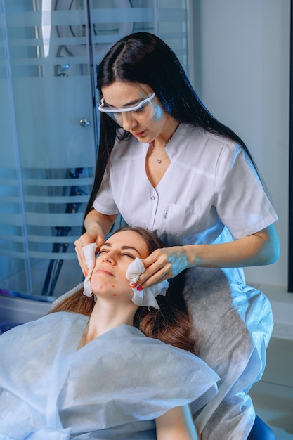 Un employé de salon de beauté traite la peau du visage d'un jeune client pour se préparer à la procédure avec une lotion.