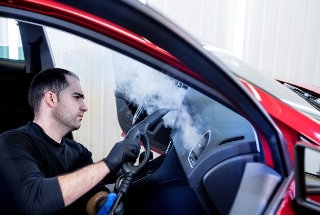 Un employé de service automobile nettoie l'intérieur avec un nettoyeur à vapeur