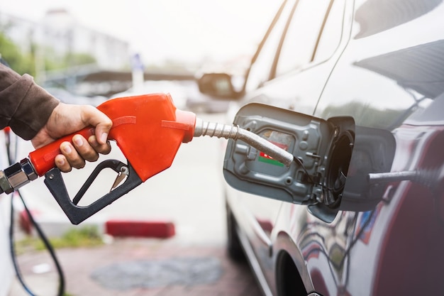 Un employé d'une station-service tient un distributeur de carburant pour remplir la voiture de carburant. La main d'un jeune homme tient une buse de gaz pour faire le plein en libre-service dans une station-service.