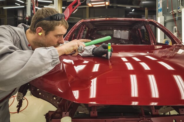 Un employé d'une usine automobile corrige un petit défaut avec un outil à main spécial