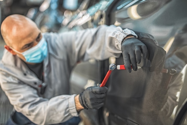 Un employé d'une usine automobile portant un masque médical de protection élimine un petit défaut métallique avec un outil à main.