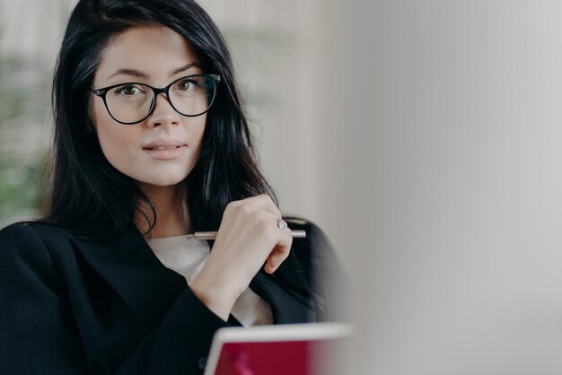 Une Employée Adulte Sérieuse Et Confiante Regarde Bien Que Des Lunettes Transparentes écrivent Des Informations Tout En Travaillant Sur Un Projet Fait Des Plans Vêtus De Vêtements De Cérémonie Note Certains Enregistrements Dans Le Bloc-notes