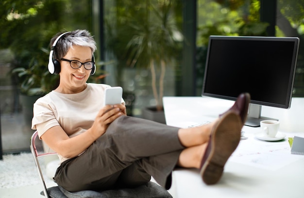 Une employée d'âge mûr et détendue fait une pause au bureau en utilisant le téléphone