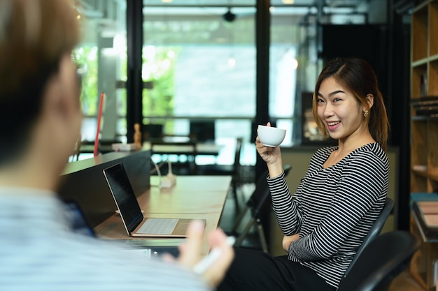 Employée asiatique amicale parlant avec son collègue pendant la pause-café au siège social