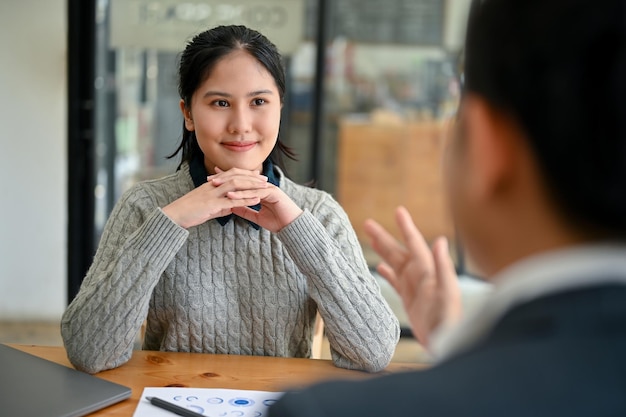 Une employée de bureau asiatique inspirée se concentre sur l'écoute de son patron la briefant sur un projet