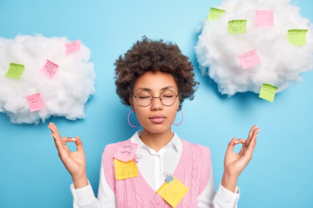 Une employée de bureau calme et relaxante se sent soulagée et médite sans stress à l'intérieur garde les yeux fermés entourés de notes autocollantes colorées