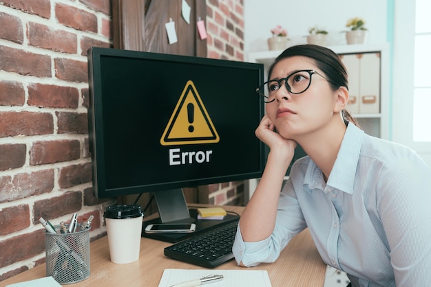 une employée de bureau déprimée assise devant un ordinateur d'erreur rêvassant pensant à une solution de travail et attendant de l'aide.