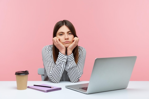 Une employée de bureau ennuyée et inefficace assise sur le lieu de travail, la tête penchée sur les mains, une femme solitaire déçue fatiguée du travail de mauviette. Studio intérieur tourné isolé sur fond rose