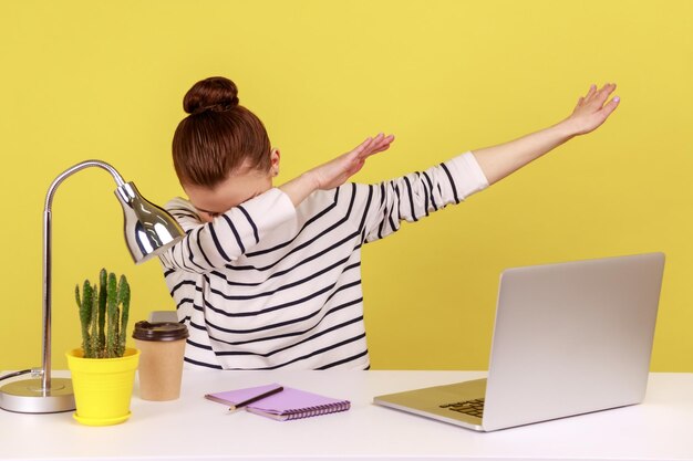 Employée de bureau extrêmement excitée assise sur le lieu de travail avec un ordinateur portable montrant un geste de danse dab