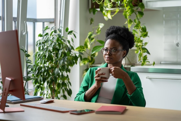 Une employée de bureau professionnelle afro-américaine faisant une pause-café est assise près de la fenêtre sur le lieu de travail