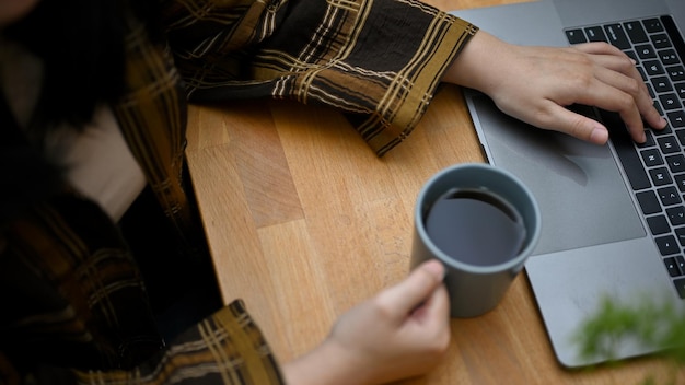 Une employée de bureau en sirotant un café tout en travaillant sur ses tâches sur un ordinateur portable à son bureau