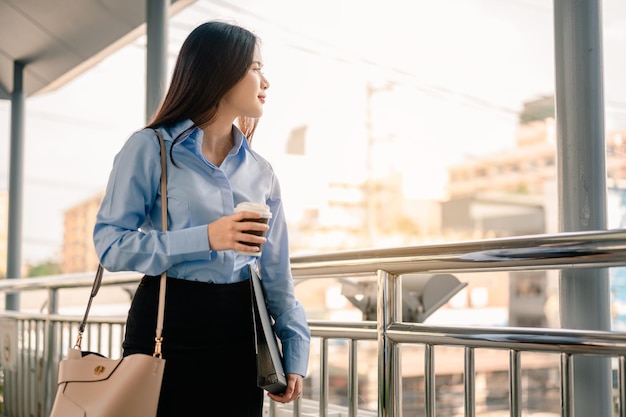 Une employée de bureau va travailler le matin avec un dossier et un café avec bonheur et fraîcheur.