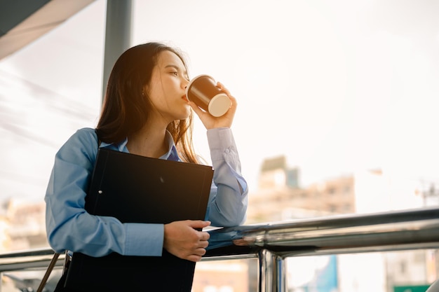 Une employée de bureau va travailler le matin avec un dossier et un café avec bonheur et fraîcheur.