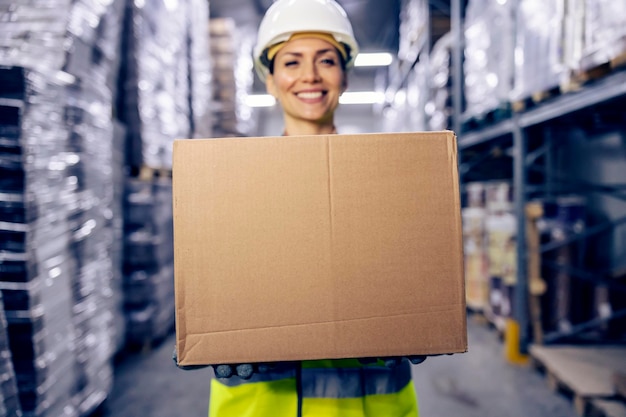 Une employée d'entrepôt heureuse transporte une boîte avec des marchandises et la prépare pour la livraison