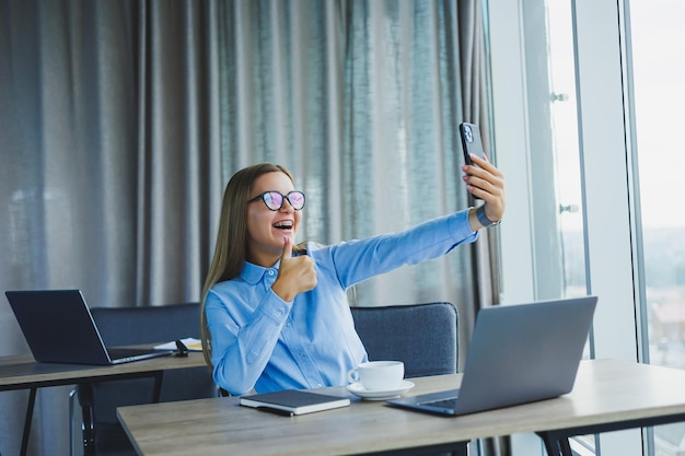 Employée intelligente avec netbook regardant la caméra pendant un appel mobile pigiste réussie en veste parlant au téléphone via l'application