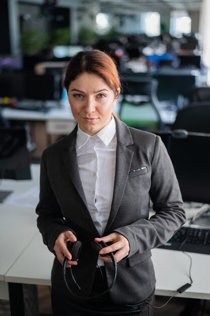 Une employée de soutien amicale dans un costume d'affaires met un casque pour commencer Heureuse femme avec un casque dans les mains travaillant dans un centre d'appels