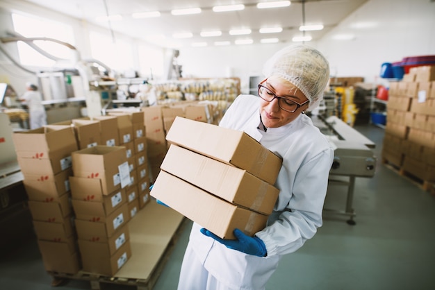 Une employée en vêtements stériles soulève de lourdes caisses en usine.