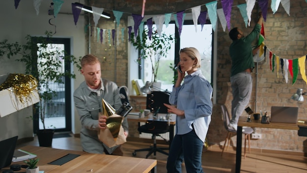 Des employés du bureau préparent une fête d'anniversaire dans une salle de travail. Un couple déballe des boîtes.