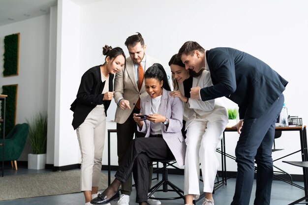 Les employés du bureau se tiennent autour d'une femme jouant sur un smartphone