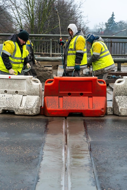 Des employés du service de la voirie en gilets jaunes spéciaux effectuent des travaux de réfection de la chaussée Restauration de la couture de déformation du pont automobile