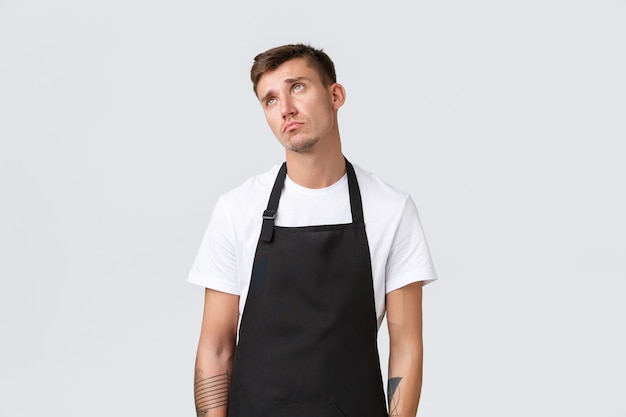 Employés, épiceries et concept de café. Barista réticent et de mauvaise humeur, le serveur souhaite passer, regardant dans le coin supérieur gauche en détresse et triste, debout sur fond blanc