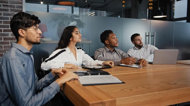 Photo employés multiethniques collègues équipe de groupe de gens d'affaires multiraciaux avec des papiers d'ordinateur portable dans la salle de conférence de bureau écouter conférence de séminaire de formation en détournant les yeux sur la présentation webinaire étude d'entreprise