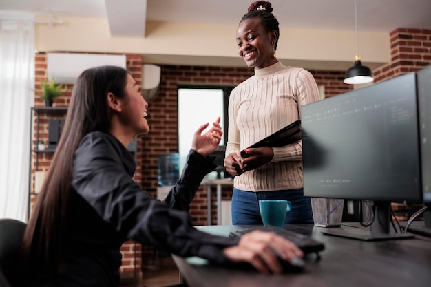 Des employés souriants et souriants de l'entreprise de développement de technologies rient d'une histoire amusante sur les pirates alors qu'ils sont assis dans un espace de travail moderne au bureau de l'ordinateur. Des collègues multiraciaux profitant d'une pause ensemble.