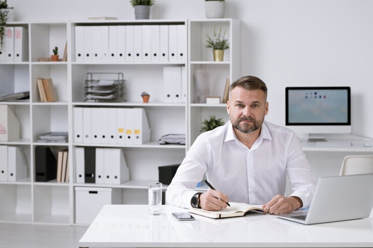 Photo employeur confiant en chemise blanche assis dans son bureau et organiser le travail tout en prenant des notes dans le cahier