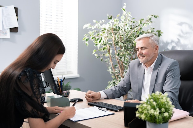 Un employeur souriant, un patron âgé et mature aux cheveux gris vêtu d'un costume, est assis dans un fauteuil