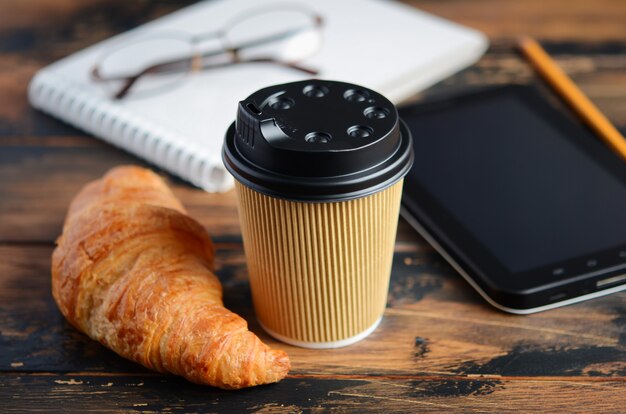 Emporter une tasse de café avec un croissant sur une table en bois.