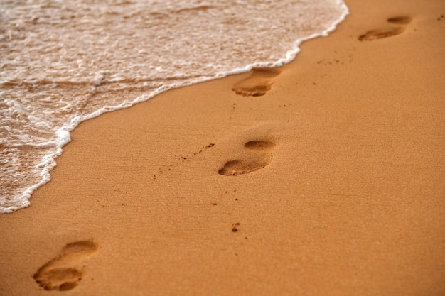 Empreintes au coucher du soleil avec vague de plage de sable doré et traces de pas en été