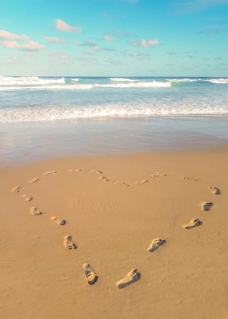 Photo empreintes de pas dans le sable en forme de coeur amour voyageant sur la plage