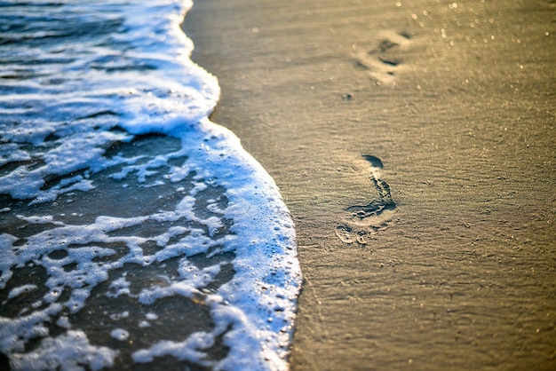 empreintes de pas sur le sable emportées par la vague coucher de soleil