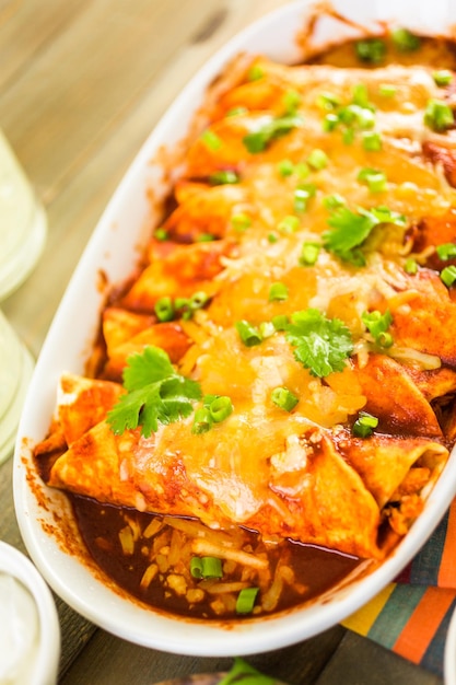 Enchiladas de poulet maison garnies d'oignons verts et de coriandre dans une cocotte blanche.