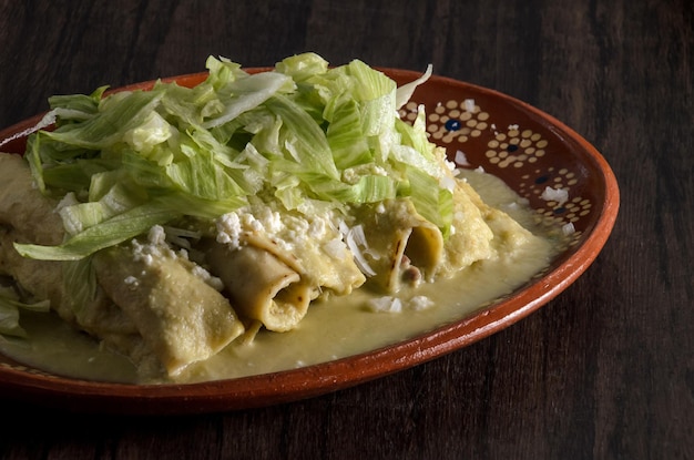 Enchiladas vertes avec de la laitue servies dans un plat en argile sur une table en bois.