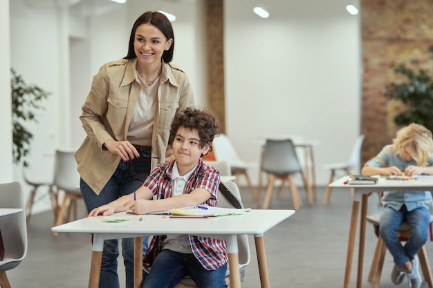 Encouragez les enfants à apprendre une jeune enseignante souriante debout près d'un petit écolier pendant la leçon