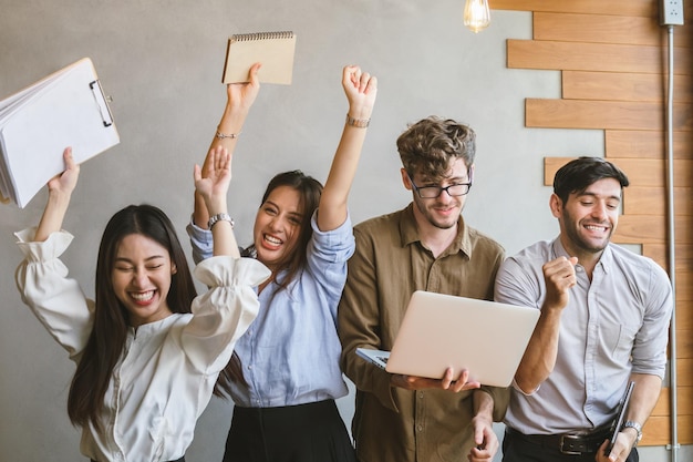 Encouragez-vous, groupe de gens d'affaires étonnés, travail d'équipe de jeunes asiatiques, caucasiens s'amusant, heureux sur le lieu de travail après la fin du projet, gagnez lors d'une conférence avec des partenaires sur un ordinateur portable. Célébration du concept de réussite.