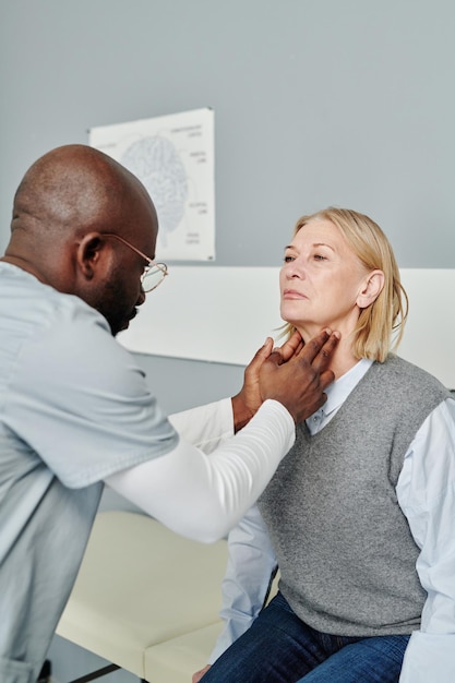 Endocrinologue afro-américain vérifiant la thyroïde d'une patiente mature