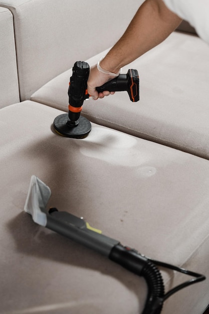 Enduire de détergent sur le canapé à l'aide d'une perceuse avec une brosse pour le nettoyage à sec Appliquer du détergent sur le canapé à l'intérieur de la maison pour le nettoyage à sec