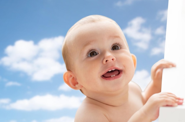 enfance, l'enfance, les émotions et les gens concept - heureux petit bébé garçon ou fille regardant vers le haut sur le ciel bleu et les nuages arrière-plan