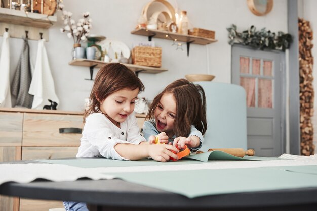 Enfance heureuse. Deux enfants jouant avec des jouets jaunes et oranges dans la cuisine blanche.