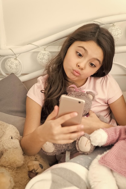 Enfance heureuse Une fille avec un smartphone utilise la technologie moderne Selfie avec son jouet préféré Envoyez une photo de selfie à votre réseau social d'amis Un enfant prenant un selfie avec des jouets et s'amusant