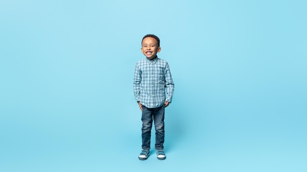 Enfance heureuse Portrait en pied d'un adorable petit garçon afro-américain souriant à l'arrière-plan bleu de la caméra
