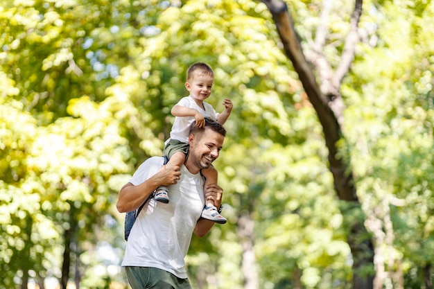 Enfance et parentalité heureuses Papa joyeux tient le garçon sur ses épaules et rit un été ensoleillé ou une journée de printemps dans la nature Une aventure dans la nature d'une famille heureuse Jouer dans le parc