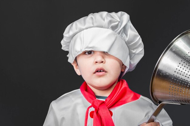 Enfance, petit garçon préparant des aliments sains dans la cuisine sur fond gris, chapeau de cuisinier