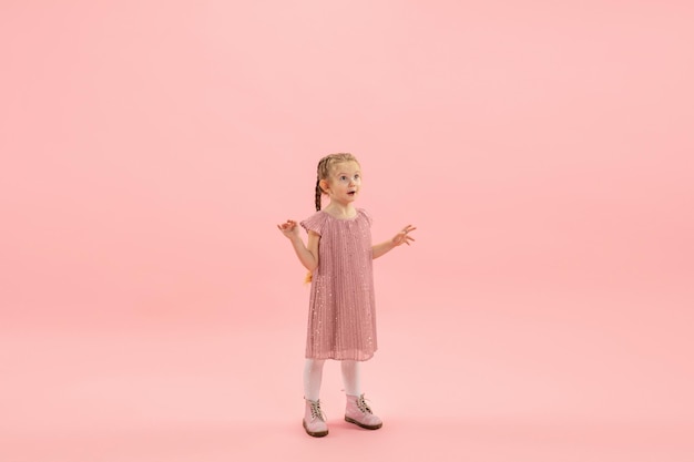 Enfance et rêve d'un avenir grand et célèbre. Jolie fille aux cheveux longs isolée sur fond rose corail