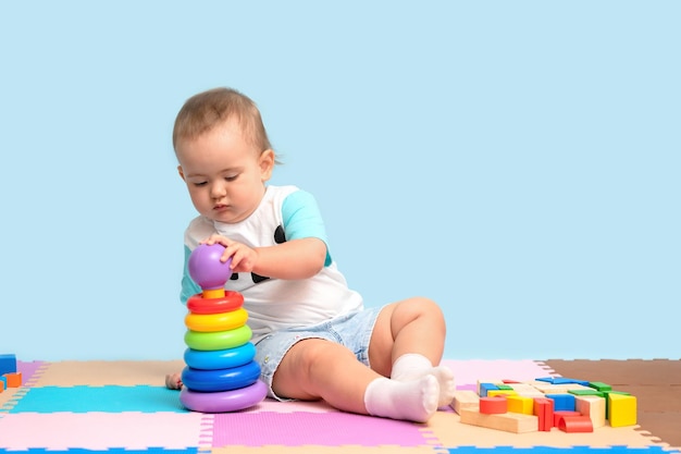 Un enfant de 1523 mois est assis et assemble un jouet pyramidal mettant des anneaux colorés sur la base en plastique de la tour